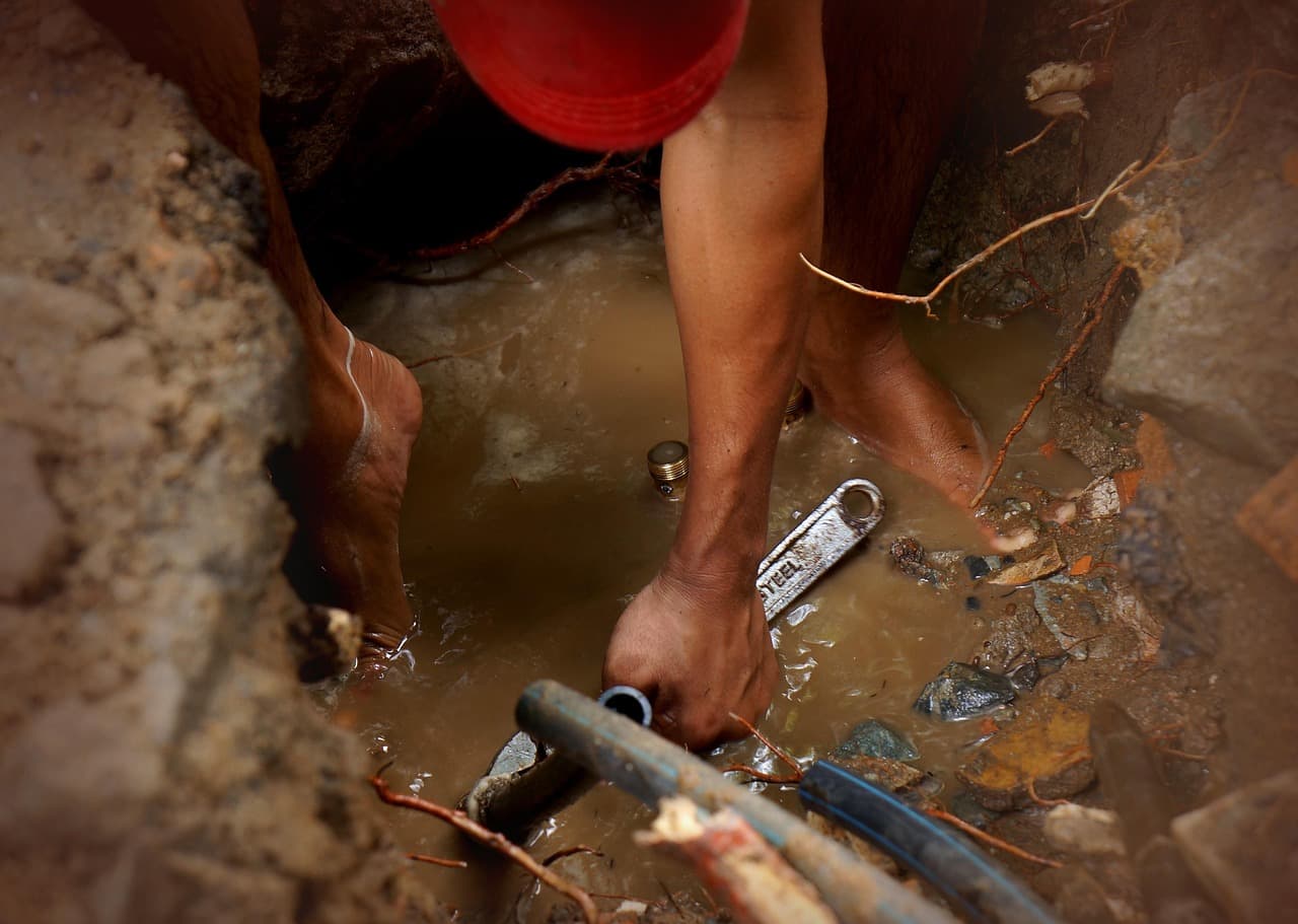 Hands repairing a pipe in a flooded drainage trench