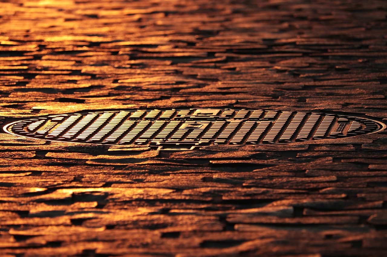 Cast-iron manhole cover set into wet cobbles at dusk
