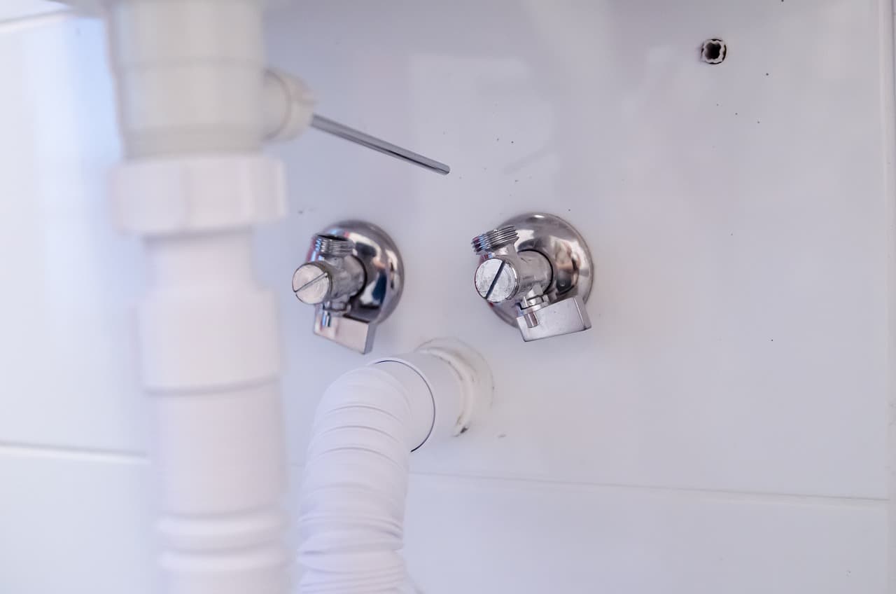 White waste pipes and chrome valves on a bathroom wall
